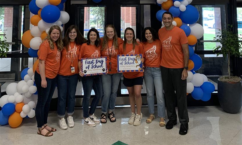A group of teachers smiles with a first day of school sign